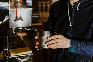 Fototapeta na wymiar Barista steaming milk in the pitcher with coffee machine preparing to make latte art in cafe
