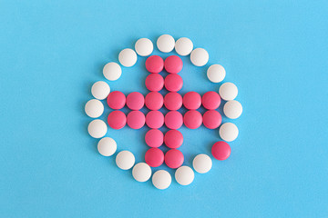 Flat lay. Group of pink and white round pills forms cross figure in circle on a blue background. Selective focus. Theme of health care, medical treatment and disease prevention.