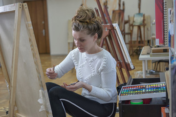 Woman artist in an art studio paints crayon painting on canvas.