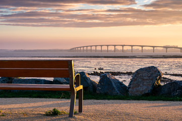 one bench with nobody on the first plan with the re island bridge at the background