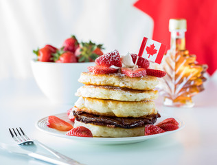 A close up of a stack of pancakes and strawberries for Canada Day with a maple leaf bottle of syrup. Canada Day concept.