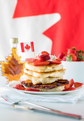 A stack of pancakes with strawberries and maple syrup against a Canadian flag background. Canada Day concept.