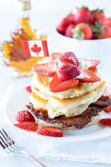 A vertical view of a stack of pancakes with strawberries and syrup to celebrate Canada Day.