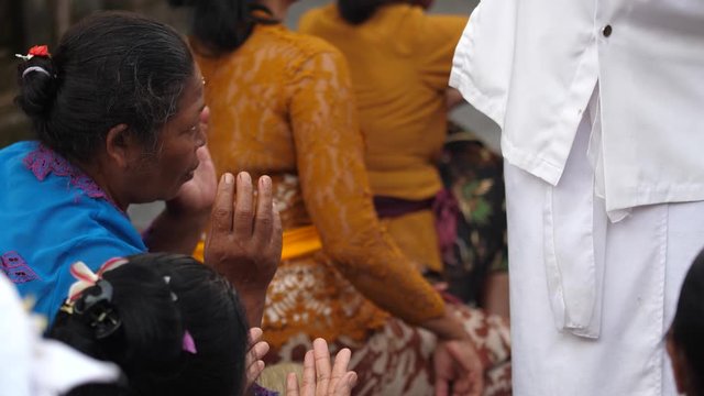 Blessing and cleansing in Hinduism as priest pours water into hands of women attending a ceremony at the temple in Ubud, Bali. Religious beliefs and Hindu culture of Indonesia.
