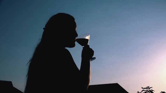 Young Woman Drinking a Cocktail Silhouetted Against the Setting Sun