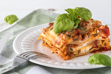 A close up of a slice of lasagna on a plate garnished with basil.