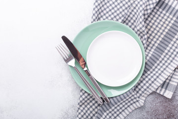 Empty mint and white plates, linen napkin, knife and fork on stone background Copy space Top view