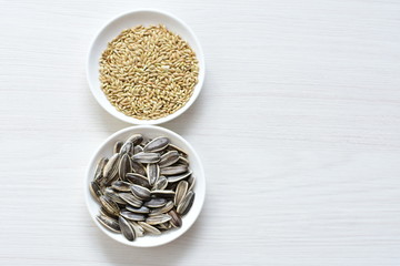 Birdseed and natural sunflower seeds, food for birds, displayed in containers on white wooden background