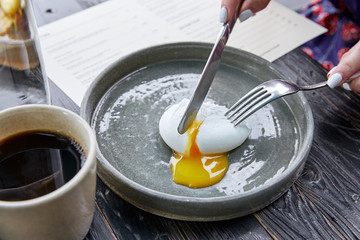 A soft-boiled egg is cut with a knife and the yolk flows on a gray plate, cup of coffee breakfast