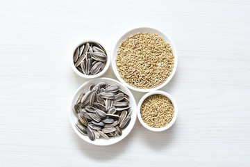 Birdseed and natural sunflower seeds, food for birds, displayed in containers on white wooden background