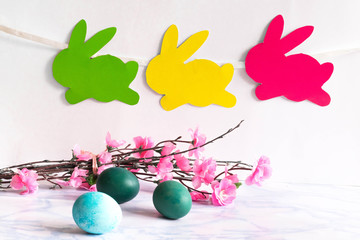 Colorful eggs with willow and handmade bunny easter garland on netural background.