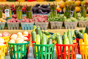 Baskets of zucchini and potatoes cover a table at local farmers market, with more fresh produce in the background