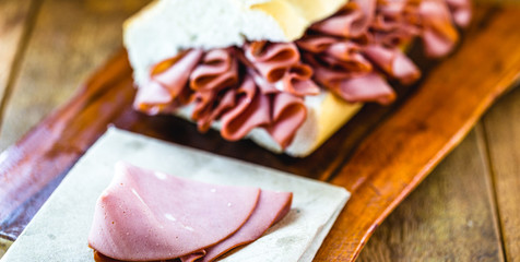 mortadella, pork slices, on italian bread, on rustic wooden background. A mortadella sandwich is...