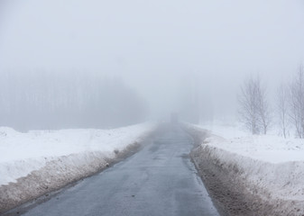 Obraz na płótnie Canvas Rural asphalt road on foggy winter day, with truck in the distance