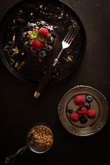 Czekoladowe babeczki z malinami i jagodami na czarnym talerzu, Moody style, Zdjęcie żywności w ciemnych kolorach, widok z góry - 329643409