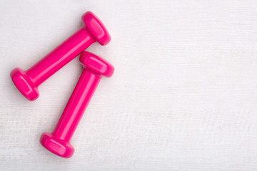 Creative flat lay overhead composition with pink female dumbbells on a light wooden background. Top view. Free copy space for text.