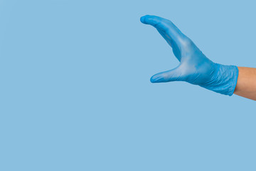 Obraz premium Doctor's hand in a blue medical glove holds an object on a blue background. infection control. mocap, you can insert your product for advertising