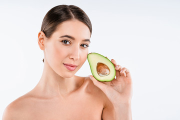 Beauty portrait of young topless woman standing isolated over white background and showing sliced avocado