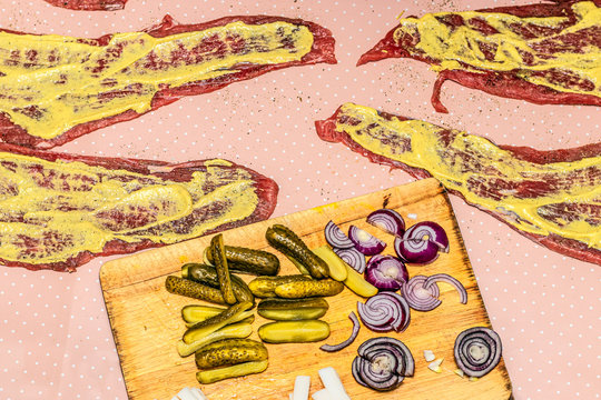 Geschnittene Gurken, Zwiebeln und Speck auf Holzbrett umgeben von vorbereiteten Rouladen, schon mit Senf bestrichen