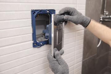 Plumber installing button for toilet bowl in restroom, work in bathroom