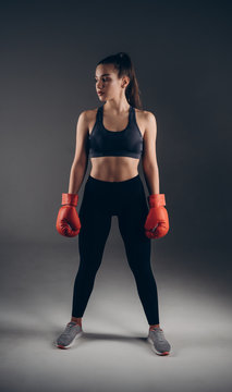 Full-leght Image of a beautiful young amazing sports fitness caucasian woman boxer posing isolated over gray background in red gloves. © Owl-vision-studio