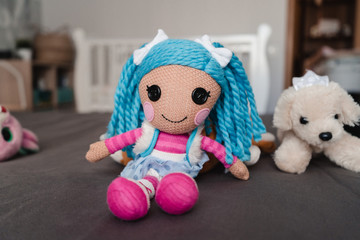 Knitted doll with blue hair. Children's toy on the crib. Crochet for kids