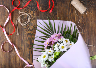 top view of beautiful bouquet in wrapping paper, ribbons on wooden table