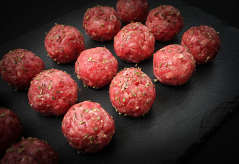 bright raw meatballs on the background of dark basalt plate