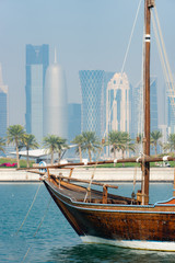Retro historical boat with blurred panoramic view of modern skyline of Doha and green palms on...