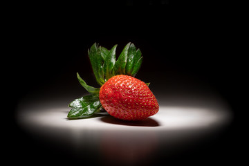 Single ripe strawberry isolated on a black and white background backlit by white light with shadows.