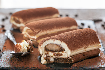 A trio of tiramisu dessert on a rectangular slate plate. A spoon with s bit of tiramisu.