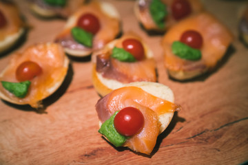 Finger food with toast, topped by salmon slices, cherry tomatoes and green paste