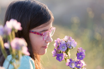 A girl is smelling flowers while on an outdoor hike.