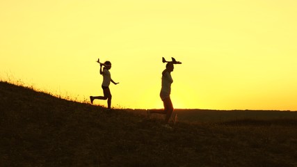 Dreams of flying. Happy childhood concept. Two girls play with a toy plane at sunset. Children on background of sun with an airplane in hand. Silhouette of children playing on plane