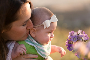A mother and her baby stop and smell the flowers on an outdoor hike.