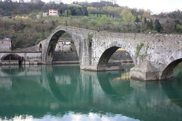 Fototapeta na wymiar The suggestive and famous Ponte del Diavolo of Lucca built in bricks over a river in an ancient medieval village in Borgo a Mozzano