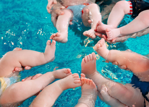 A group of mothers with their young children in a children's swimming class with a coach.