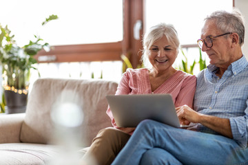 Mature couple using a laptop while relaxing at home - obrazy, fototapety, plakaty