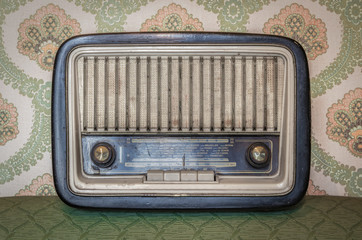 An old transistor radio, with knobs and buttons for manual tuning. In the background a vintage...