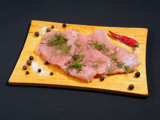 Sliced pieces of meat turkey game filet, fennel, allspice, red chili pepper, salt on a wooden cutting board on black wooden background. Healthy eating concept