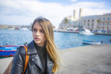 Fototapeta premium Giovane donna italiana nei pressi del porto turistico di Molfetta con Duomo nello sfondo di cui si vedono i due campanili e barche da pesca 