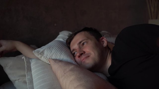 Handsome young man resting on bed in early morning. Portrait of smiling male looking away while lying on pillows in bed.