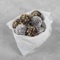 Vegan energy balls made from dried prunes, dates, dried apricots and almonds, cashews, walnuts, with nut and coconut topping on a plate on a light background