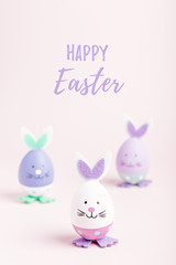Funny cute bunny eggs in pastel colors on pink table top, Easter holiday concept. Easter decoration for kids still life, copy space