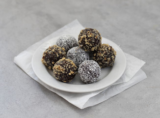 Energy candy balls made from dried prunes, dates, dried apricots and almonds, cashews, walnuts, with nut and coconut topping on a plate on a light background