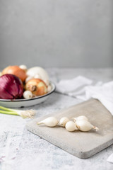 Whole Pearl Onions on Cement Cutting Board with Several Varieties of Onions Out of Focus in Background
