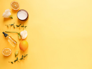 flatlay composition with cream, oil, flower, citrus and eucalyptus on yellow background. Concept...