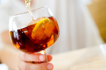 hand pouring ice tea in glass with slice of lemon