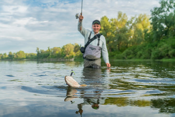 Pike fishing. Fisherman catch fish in water at river