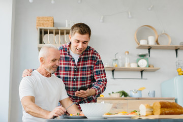 Young man and senior father using phone in the kitchen